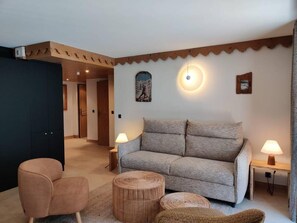 A cozy living room with a sofa, two side tables with lamps, a round wicker ottoman, and a chair.