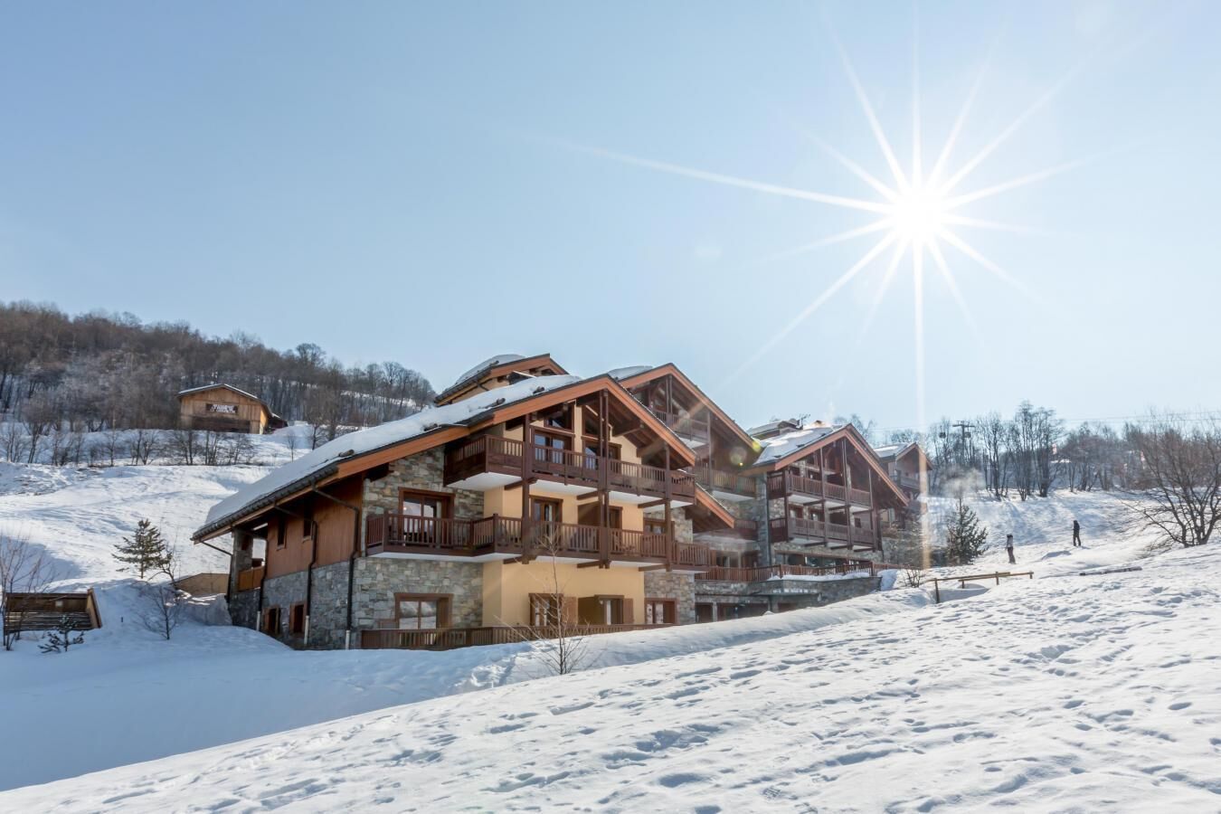 A multi-story chalet with balconies, set on a snowy slope with a clear sky.