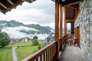 A wooden balcony with a stone wall, overlooking a mountainous landscape with houses and a path. - 50m from ski slopes, 5th floor, view valley, fitness, swimming pool, sauna, hammam, balcony, tv (Saint-Martin-de-Belleville)