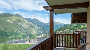 A wooden balcony with a view of a village and mountains.