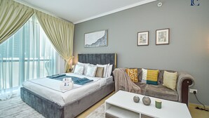 Ett modernt sovrum med en stor säng, en soffa och ett litet bord. Det finns gardiner vid fönstret och konstverk på väggen.