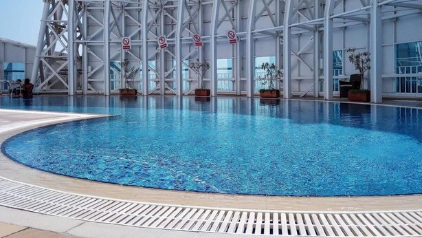 En stor inomhuspool med en modern arkitektonisk bakgrund, omgiven av planterade växter och ett metallräcke.