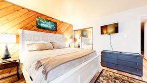 A bedroom with a wooden ceiling, a bed with a white headboard, a TV mounted on the wall, and a dresser. - Pet-Friendly, Bright Modern Gem, Gas Grill, Near Trails, Quiet Location (Mammoth Lakes)