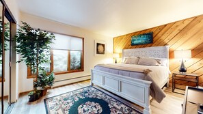 A bedroom with a large bed, a wooden sloped ceiling, a window, and a potted plant. - Pet-Friendly, Bright Modern Gem, Gas Grill, Near Trails, Quiet Location (Mammoth Lakes)