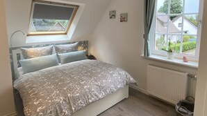 A bedroom with a bed, a skylight, a window with curtains, and a radiator. - Worpsweder Blick (Osterholz-Scharmbeck)