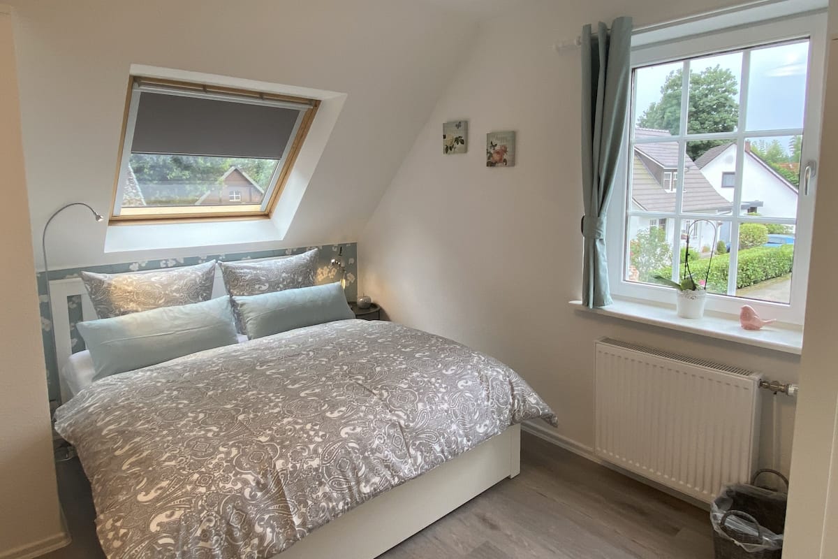 Ein Schlafzimmer mit Bett, Oberlicht, Fenster mit Vorhängen und Heizkörper.