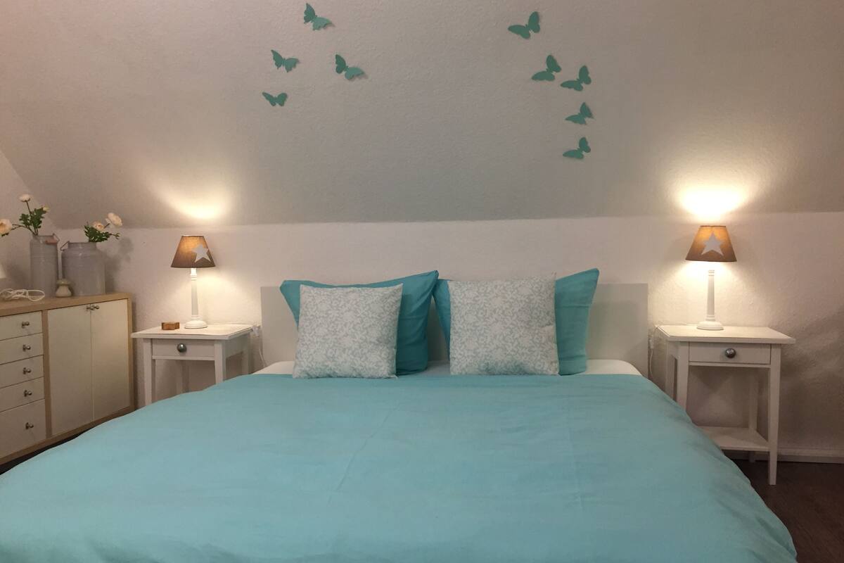 Ein Schlafzimmer mit einem Bett, zwei Nachttischen, einer Kommode und Wandstickern mit Schmetterlingsmotiven.