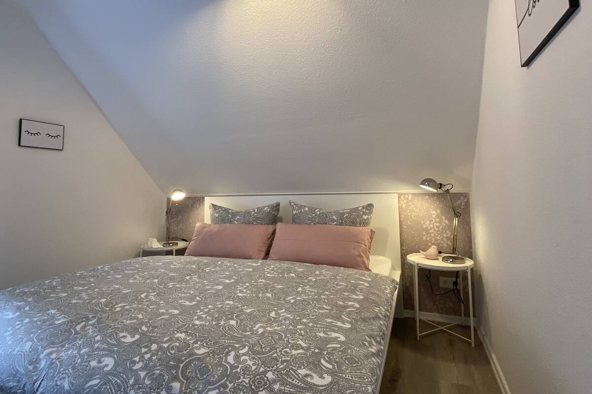 Ein Schlafzimmer mit einem Bett, zwei Nachttischen, einer Wanduhr und einem gerahmten Bild.