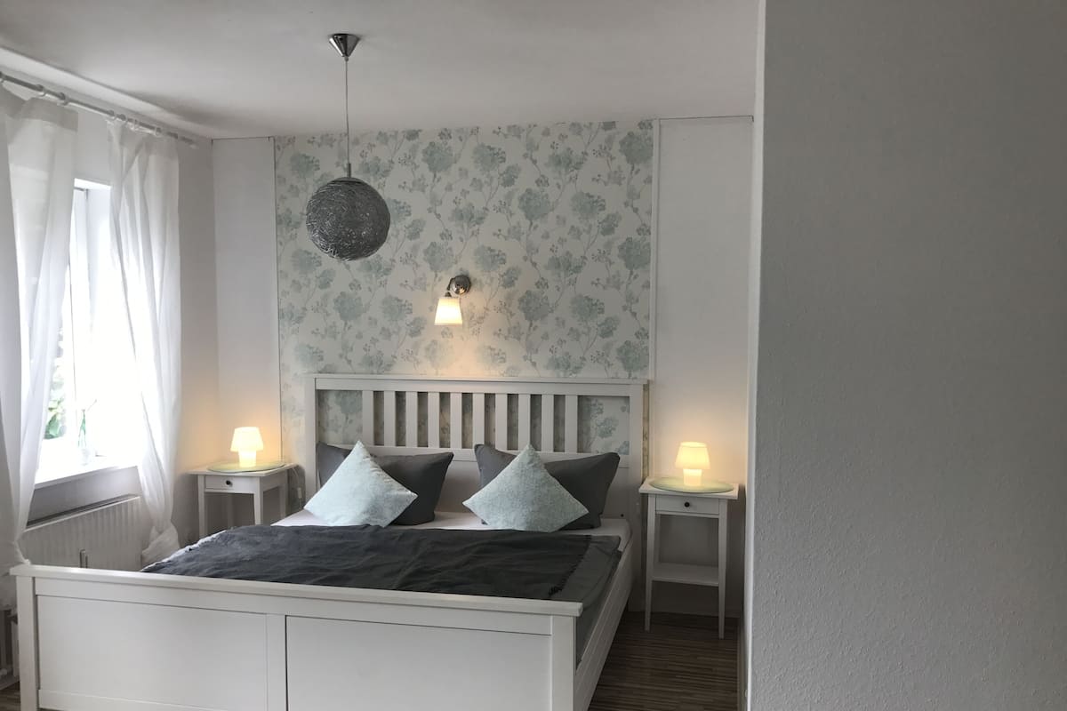 Ein Schlafzimmer mit einem Bett, zwei Nachttischen, einer Pendelleuchte und einer Wandlampe.