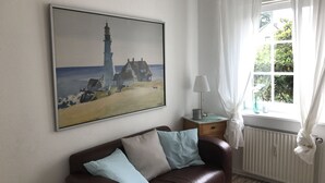 A room with a brown leather sofa, a painting of a lighthouse, a lamp, and a window with curtains. - Worpsweder Blick (Osterholz-Scharmbeck)