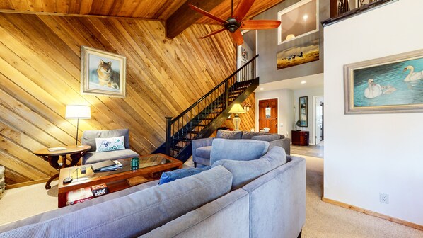 Ein geräumiges Wohnzimmer mit Holzboden, einem grauen Sofa, einem Couchtisch aus Holz und einer Treppe, die zu einer oberen Ebene führt.