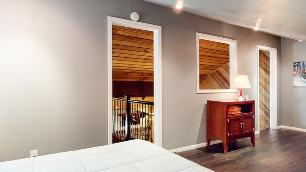 A bedroom with a wooden ceiling, a white bed, a nightstand with a lamp, and a wooden wardrobe.