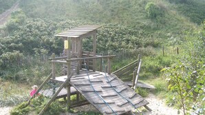 Une structure de jeu en bois, dotée d’un toboggan et d’éléments d’escalade, entourée d’une clôture et de végétation.