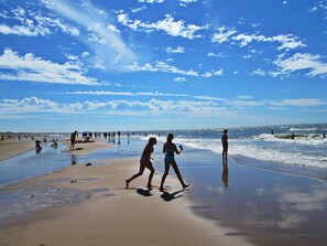 Une plage où l’on voit des gens se promener et nager, sous un ciel dégagé.