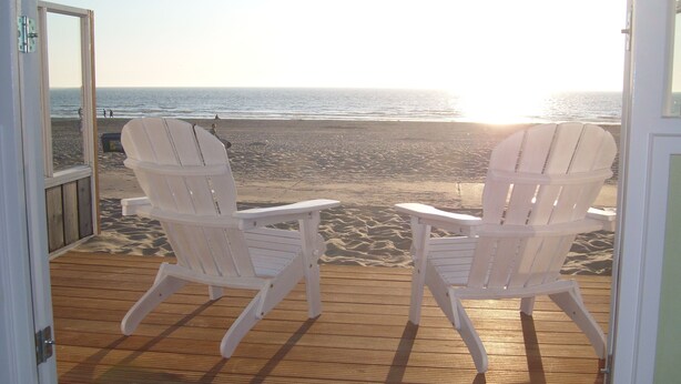 Deux chaises Adirondack blanches, placées face à une plage et à une terrasse en bois.