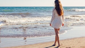 Une personne se tient sur une plage, avec des vagues en arrière-plan.