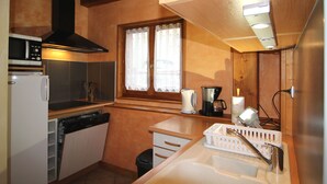 A compact kitchen with a microwave, oven, and dishwasher. There is a window with lace curtains, a sink, and a countertop with a kettle and coffee maker. - Crève Tête 3 rooms 60 m2 200 m from the free bus stop and 300 m from the ski lift (LES AVANCHERS VALMOREL)
