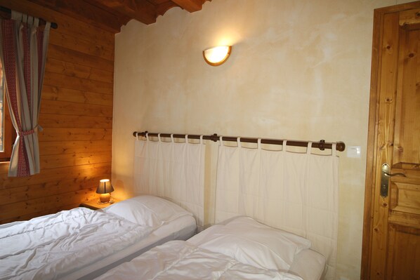 Een kamer met twee bedden, houten wanden, een nachtkastje met een lamp en een deur.