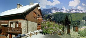 Een houten chalet met een gevel van steen, een balkon en uitzicht op besneeuwde bergen.