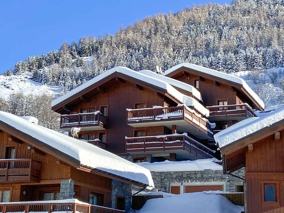 A multi-story wooden chalet with balconies, set against a snowy mountain backdrop.