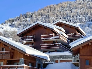 Ein mehrstöckiges Holzchalet mit Balkonen vor einer verschneiten Bergkulisse.