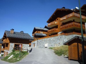 Ein mehrgeschossiges Holzgebäude mit Balkonen, einer Steinmauer und blauem Himmel.