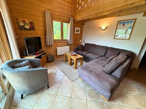 A cozy living room with a grey armchair, a large grey sofa, and a wooden coffee table. There is a television on a wooden stand and a window with curtains. - 300m from ski lifts, 2nd floor, balcony, tv, ski locker, 71m², Les Menuires (Saint-Martin-de-Belleville)