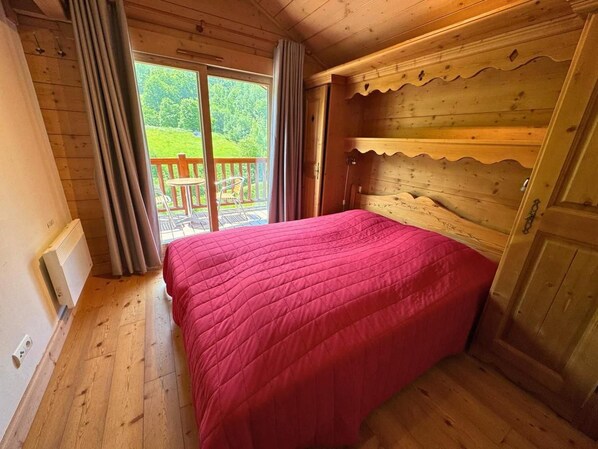 A wooden room with a bed, a radiator, and a view of greenery outside.