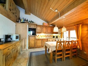 A wooden interior with a dining table, chairs, a kitchen area with cabinets, a microwave, and a hanging light fixture.