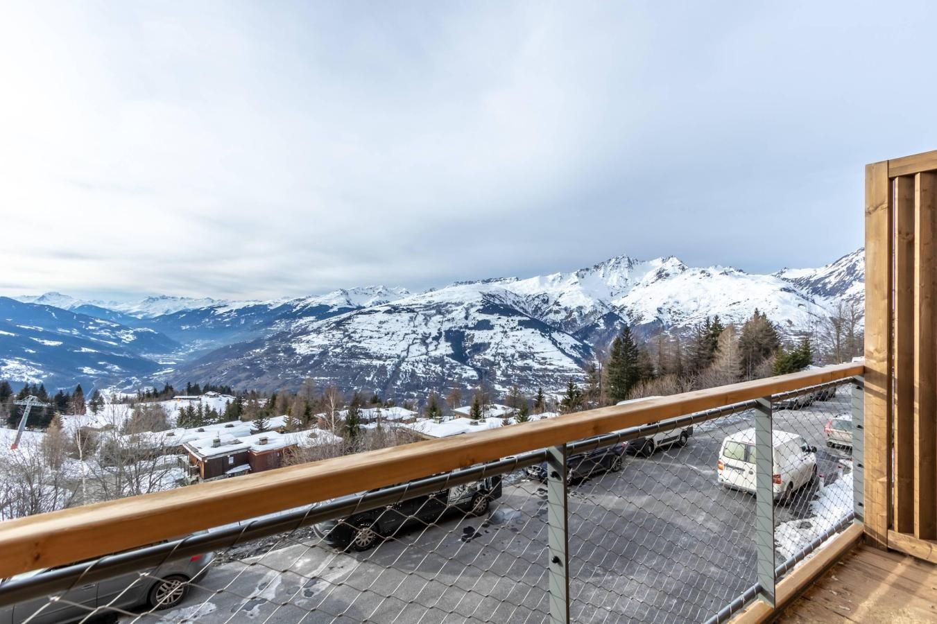 A balcony with a view of snow-covered mountains and a parking area.