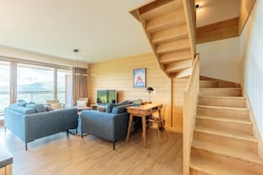 A modern living room with a wooden staircase, a large window with a view, and a flat-screen TV. - 50m from ski slopes, 3rd floor, view valley, fitness, swimming pool, sauna, hammam, balcony (Bourg-Saint-Maurice)