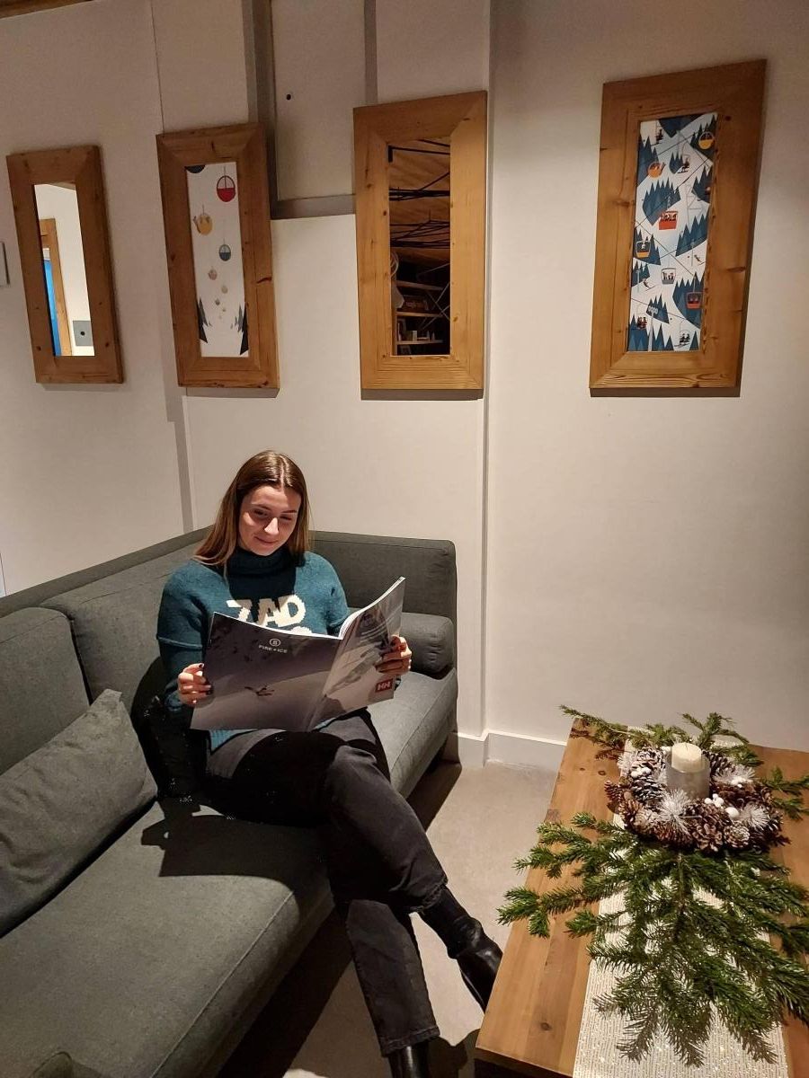 A person seated on a grey sofa, reading a book. There is a wooden coffee table with a pine branch decoration.