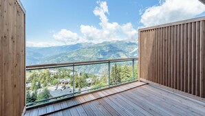 En balkon med trægulv og glasgelænder, der giver udsigt over et bjerglandskab.