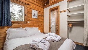 Une chambre à coucher aux murs lambrés, comprenant un lit, une fenêtre, une porte et une armoire intégrée.