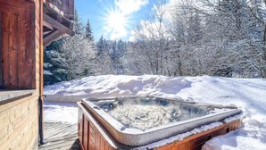 Une cabane en bois avec un bain à remous, entourée d’arbres couverts de neige.