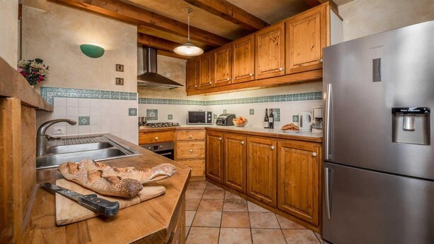 A kitchen with wooden cabinets, a stainless steel refrigerator, and a countertop with a loaf of bread and a knife. - Chalet, 200m from ski slopes, terrace, fireplace or stove, parking, tv, ski locker, 160m², La Tania (Courchevel)