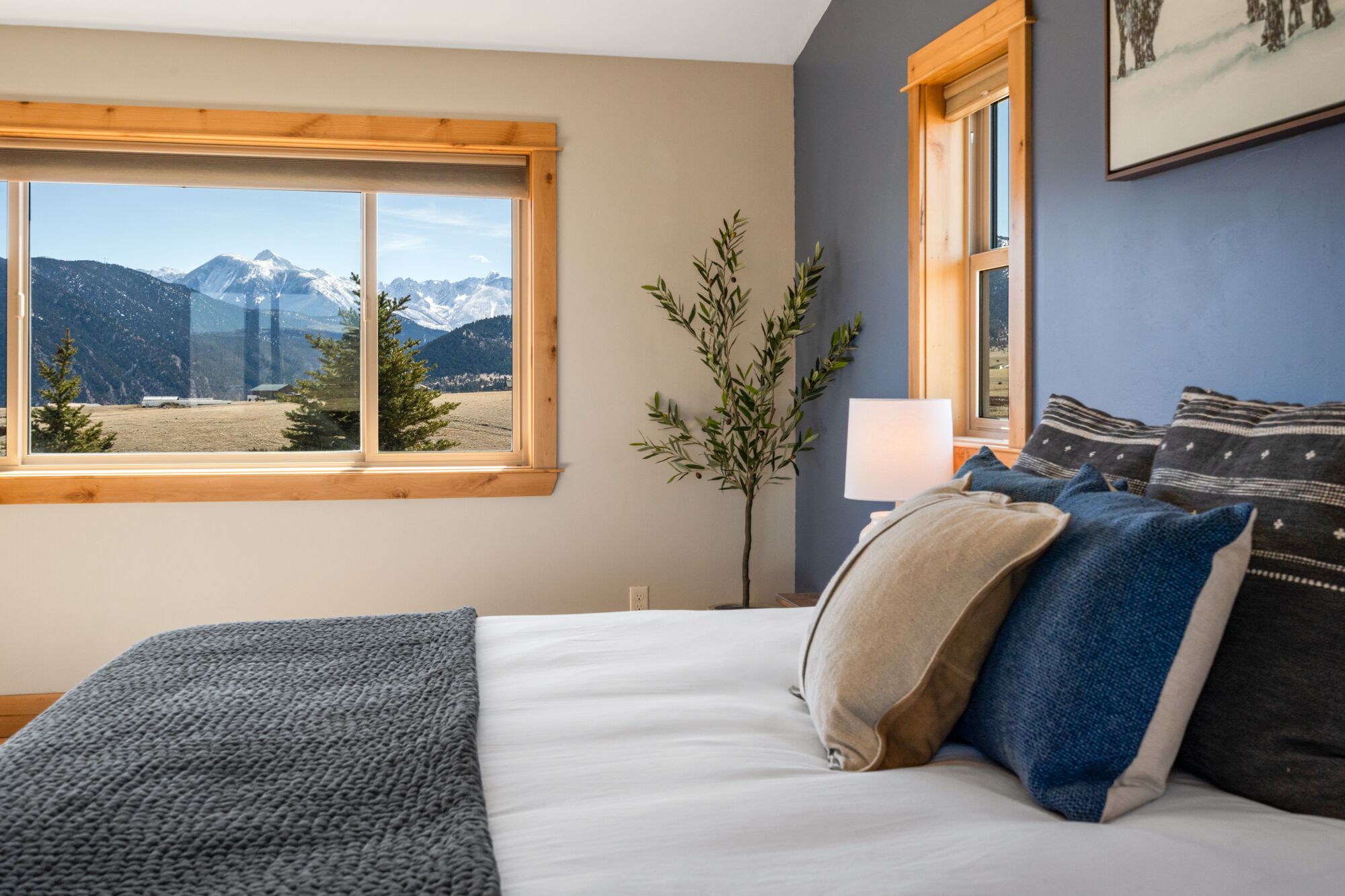 Une chambre avec un grand lit, une fenêtre donnant sur la montagne, une lampe de chevet et un tableau accroché au mur.