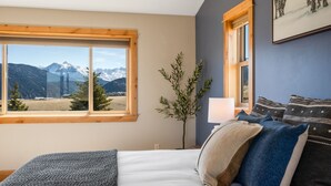 Een slaapkamer met een groot bed, een raam met uitzicht op bergen, een bedlampje en een schilderij aan de muur.