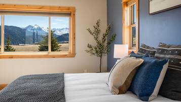 Une chambre avec un grand lit, une fenêtre donnant sur la montagne, une lampe de chevet et un tableau accroché au mur.