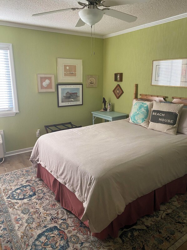 A bedroom with a bed, a ceiling fan, a nightstand, a small table, and a rug. - Discover a unique vacation experience in Myrtle Beach at Ocean Forest (Myrtle Beach)