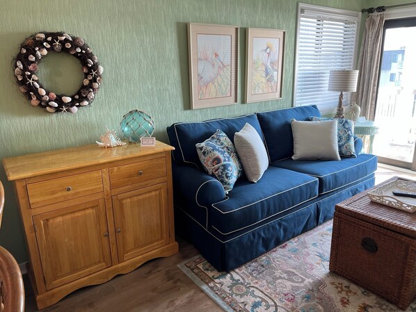 A living room with a blue sofa, wooden cabinet, and a decorative wreath on the wall. - Discover a unique vacation experience in Myrtle Beach at Ocean Forest (Myrtle Beach)