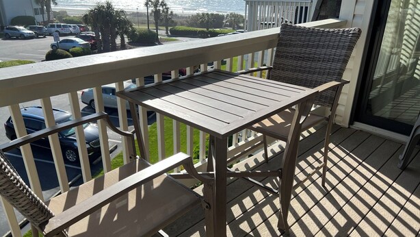 Ein Balkon mit Holztisch und -stühlen, der auf einen Parkplatz und den Blick auf das Meer zeigt.