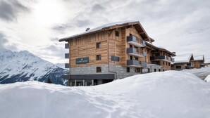 A multi-story wooden lodge with balconies, named 'Alpen Lodge', set against a snowy mountain backdrop. - Wifi, ski-in/ski-out & foot of the slopes, view mountain, fitness, swimming pool, sauna, hammam (La Rosière Montvalezan)