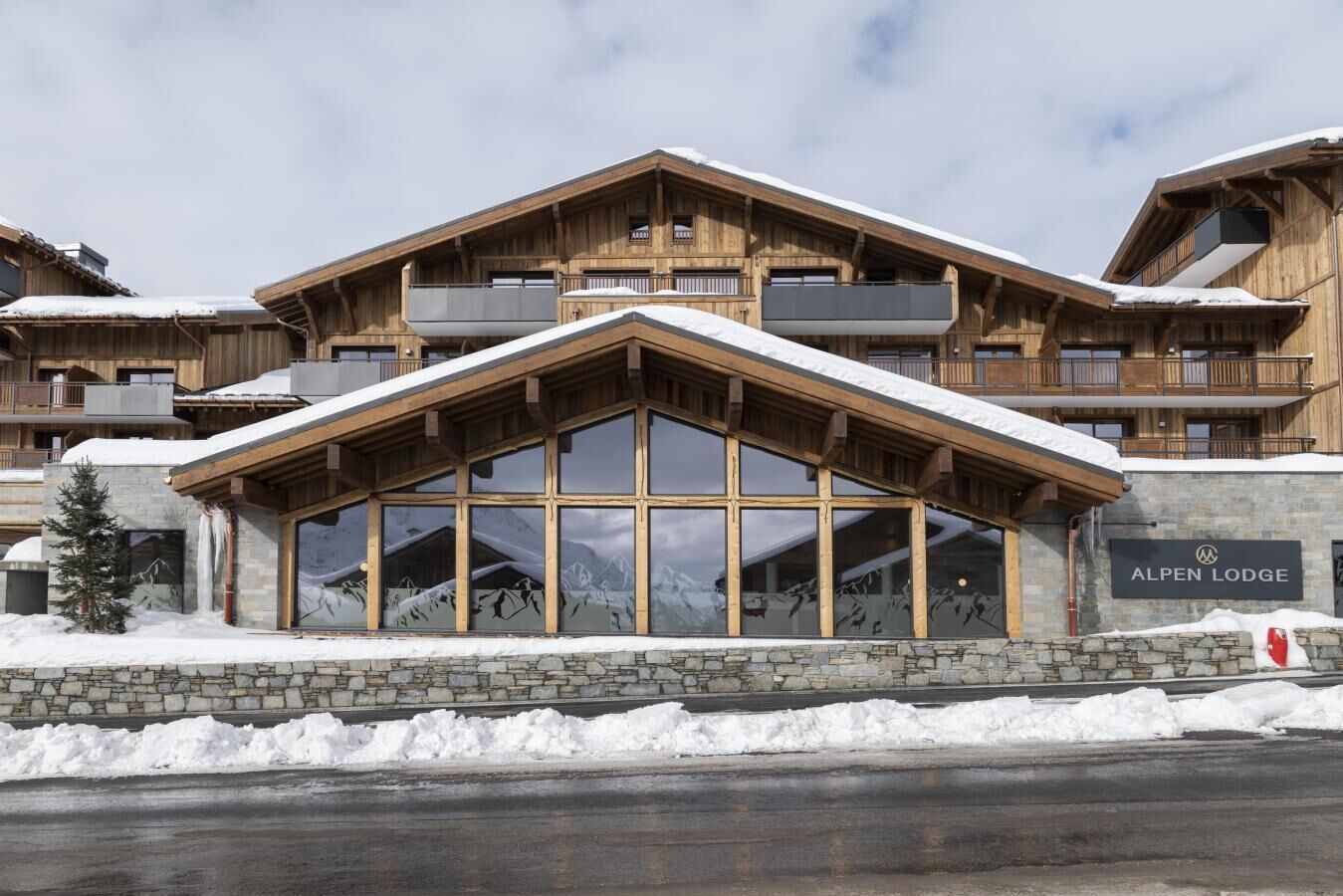 En stuga byggd av trä med stora fönster och en skylt med texten ”ALPEN LODGE”.