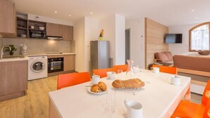 A modern kitchen with built-in appliances, a dining area with orange chairs, and a living space with a TV and seating. - 50m from ski slopes, balcony, tv, ski locker, 84m², Serre Chevalier (Briançon)