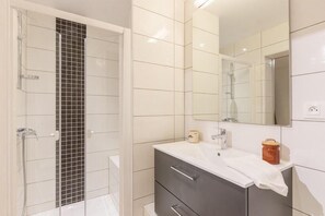 Bathroom features a shower area with a glass door and a vanity with a mirror and storage.