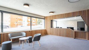 Moderni vastaanottoalue, jossa on puupanelointi, vastaanottotiski sekä oleskelualue, jossa on penkki ja tuoleja.
