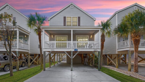 A beachfront property with two-story houses, a covered parking area, and palm trees. - 4BR Cottage with Private Pool & Walk to Beach (Surfside Beach)