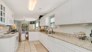 A kitchen with white cabinets, a granite countertop, a coffee station, and a view of the outdoors. - 4BR Cottage with Private Pool & Walk to Beach (Surfside Beach)