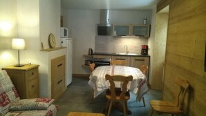 Espaço compacto com cozinha compacta, área de jantar com mesa e cadeiras, sofá e mesa de cabeceira com luminária.